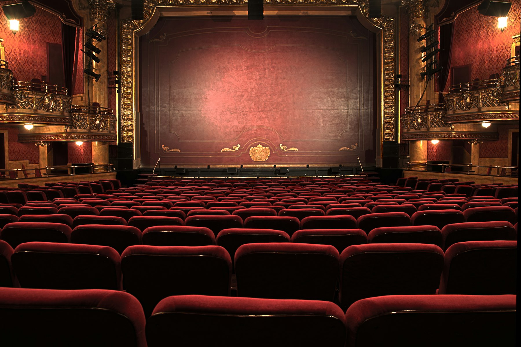 Platea di un teatro storico con poltrone rosse rivolte verso il sipario chiuso